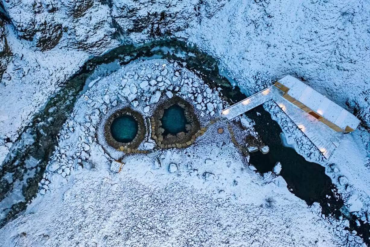 Snowy aerial view of Húsafell Canyon Baths tucked into a narrow canyon.