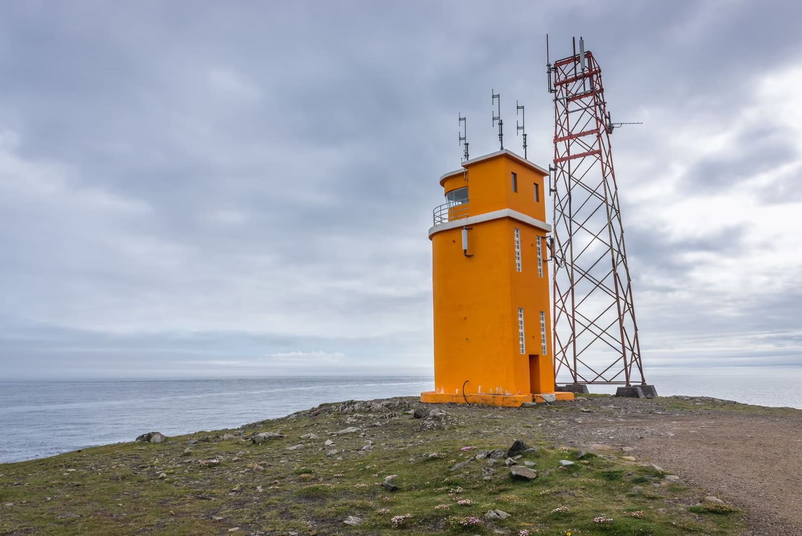 Hvalnes Lighthouse on a low headland with dark shoreline and Eystrahorn rising behind it.