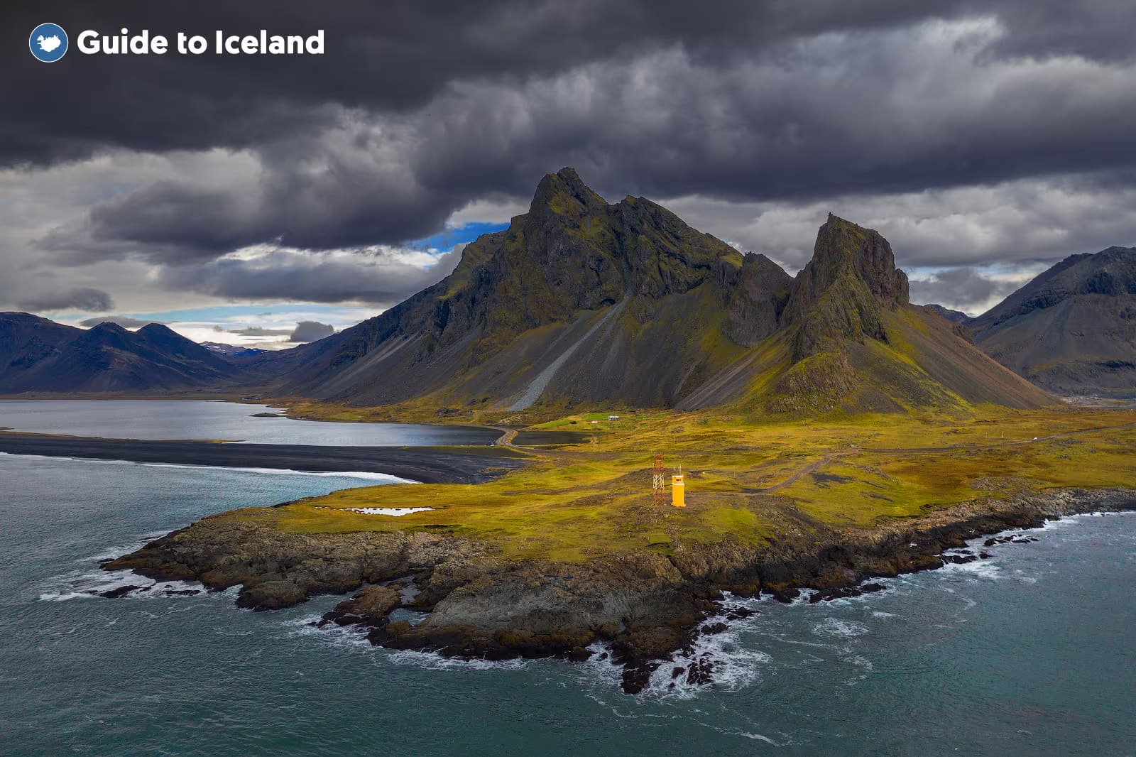 An orange Hvalnes Lighthouse standing out against the dark coastal landscape in east Iceland.