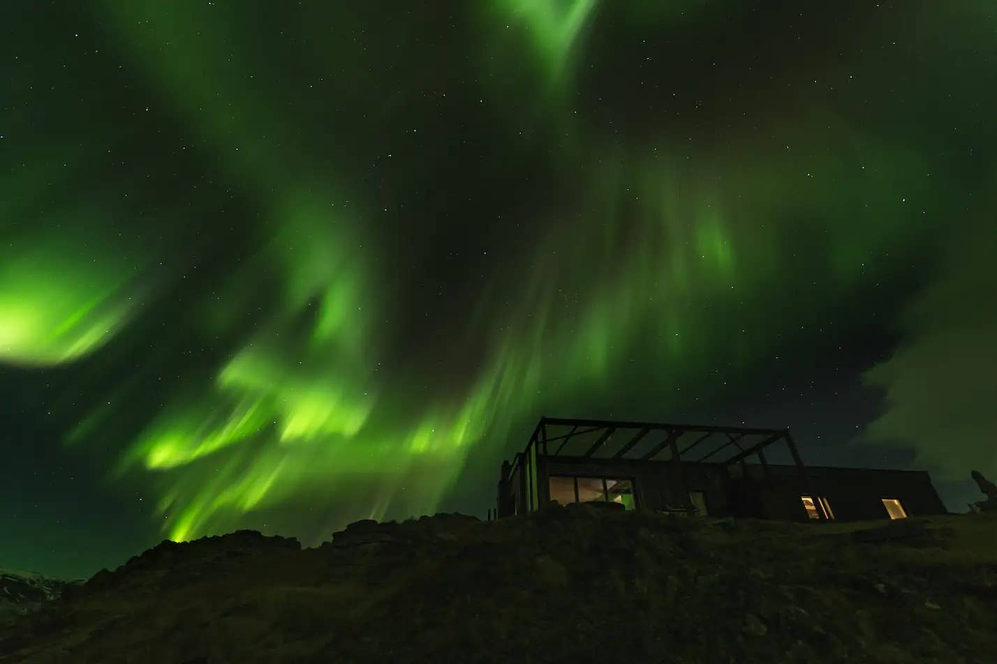 Hvammsvik Hot Springs in winter light with snow, dark fjord water, and aurora above the pools.