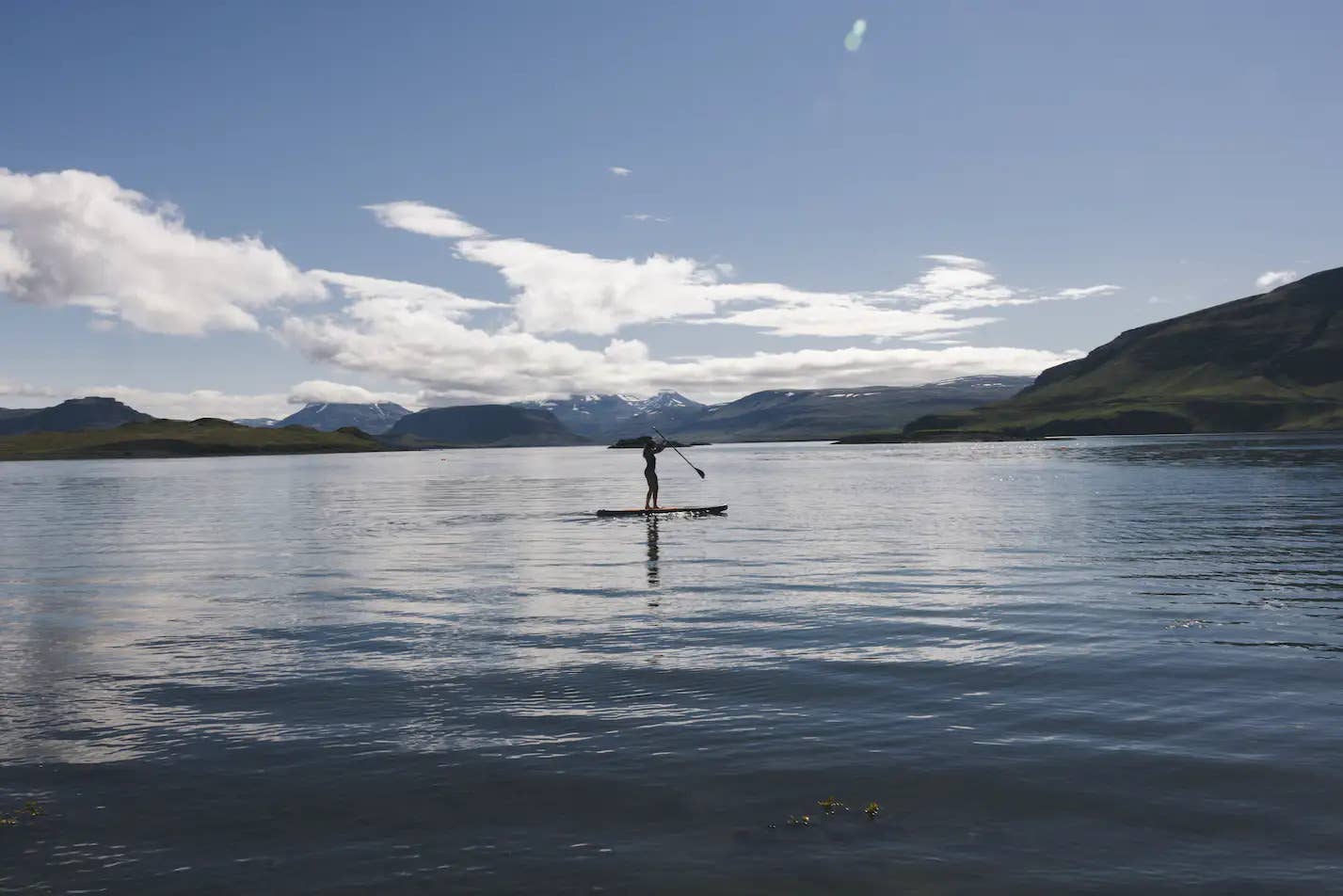 Paddleboarder on the water at Hvammsvik with the hot-spring shoreline nearby.