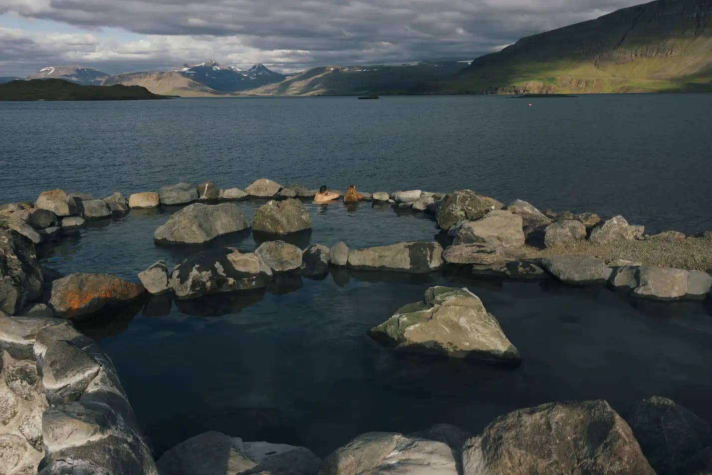 Hot pools at Hvammsvik beside the Hvalfjordur shoreline and surrounding mountains.