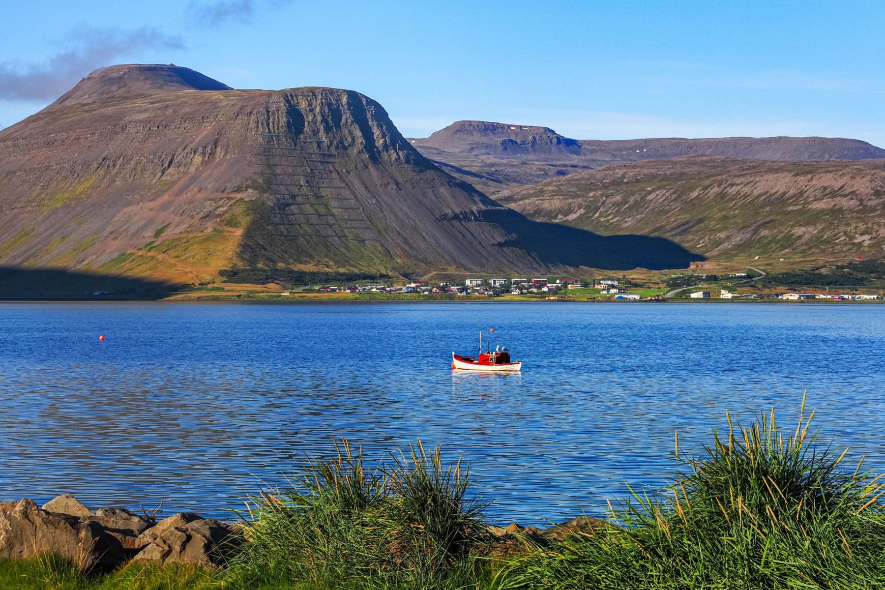 Fishing boat on Ísafjörður fjord with town buildings and Westfjords mountains reflected in calm water.