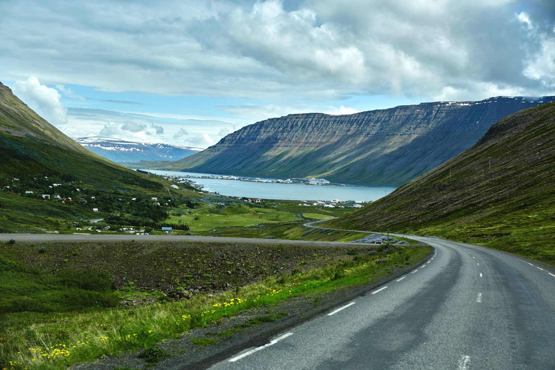 Scenic road above Ísafjörður fjord with green slopes, water, and Westfjords mountains.