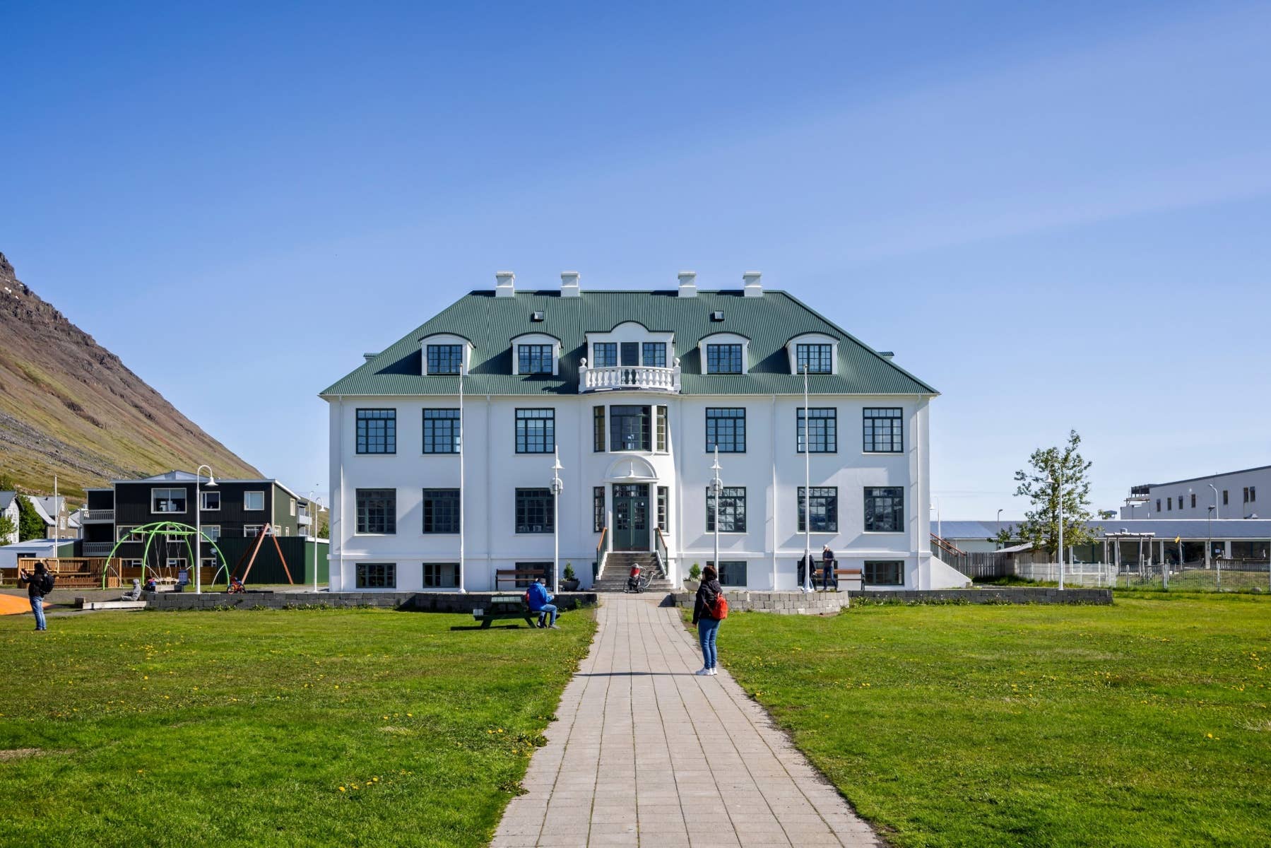Cultural building in Ísafjörður town center with a lawn, walking path, and mountains behind.