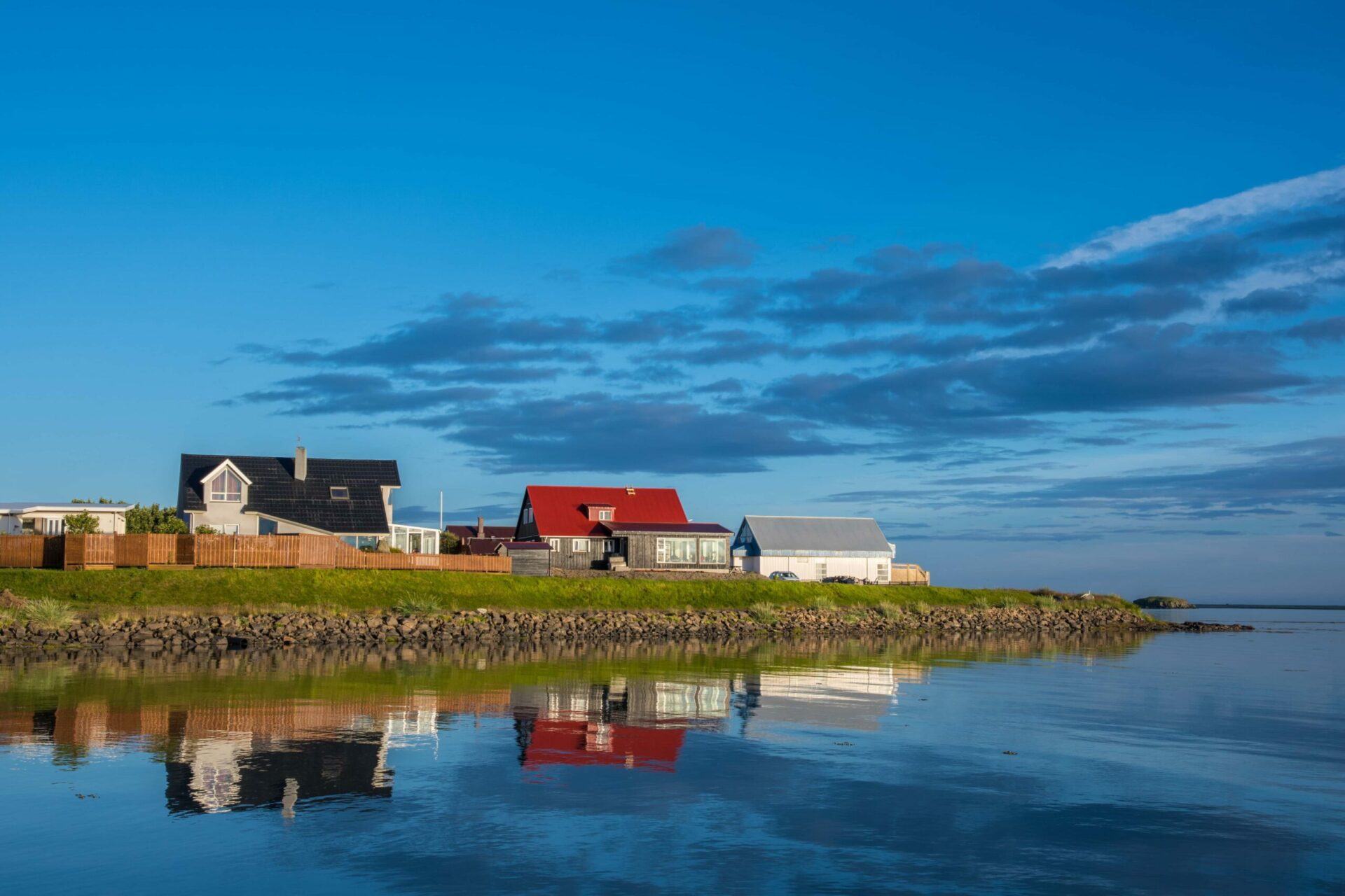 Colorful houses reflected in still water along the Hofn shoreline.