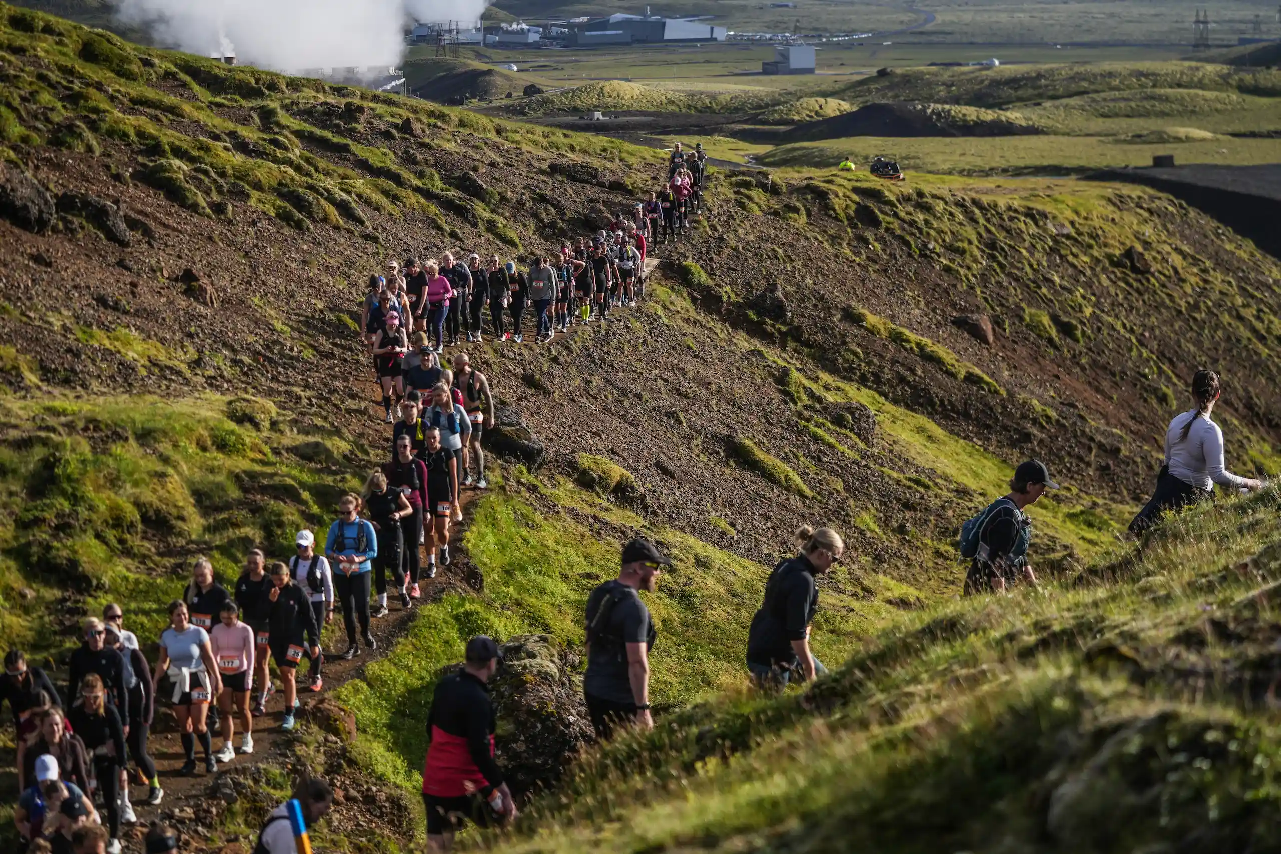 Hikers crossing green volcanic slopes in the Hengill area near Hellisheiði.