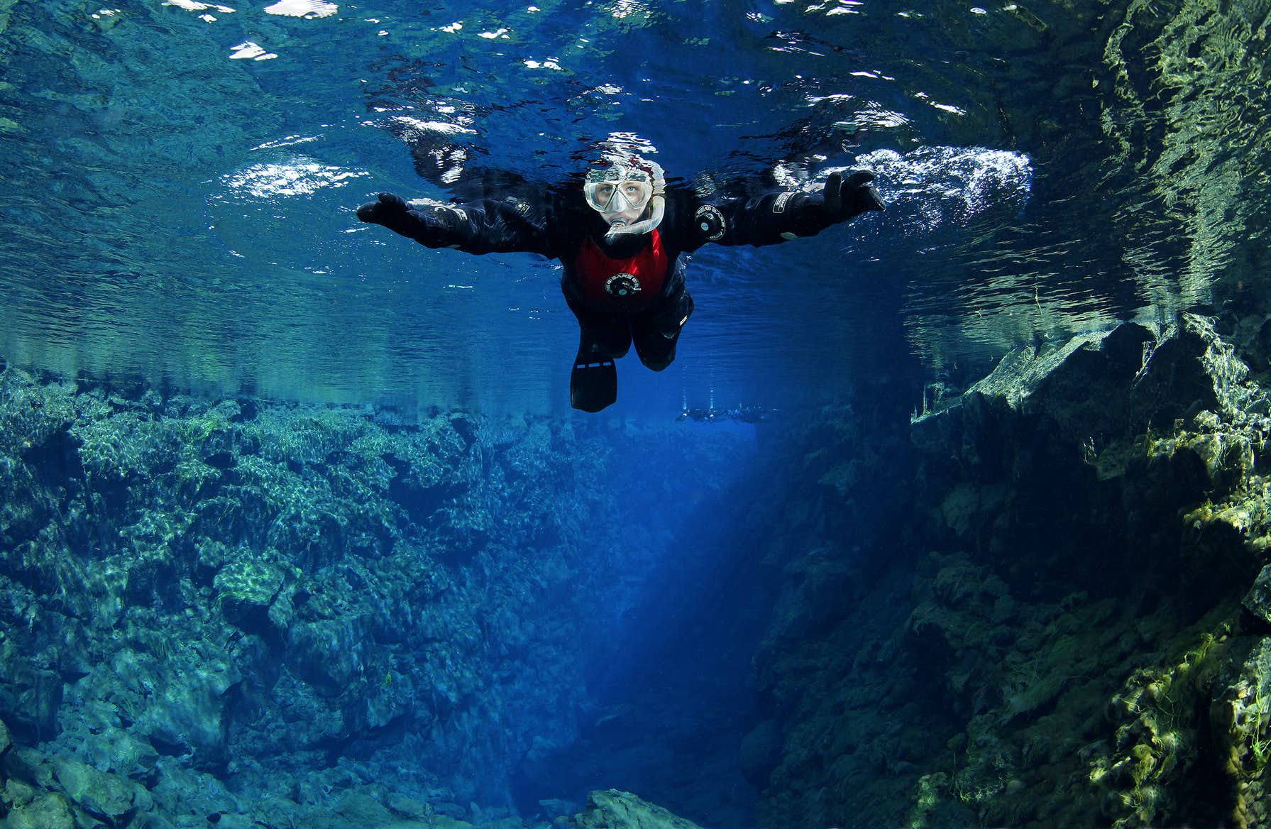Snorkeler floating between rock walls in the clear water of Silfra fissure.