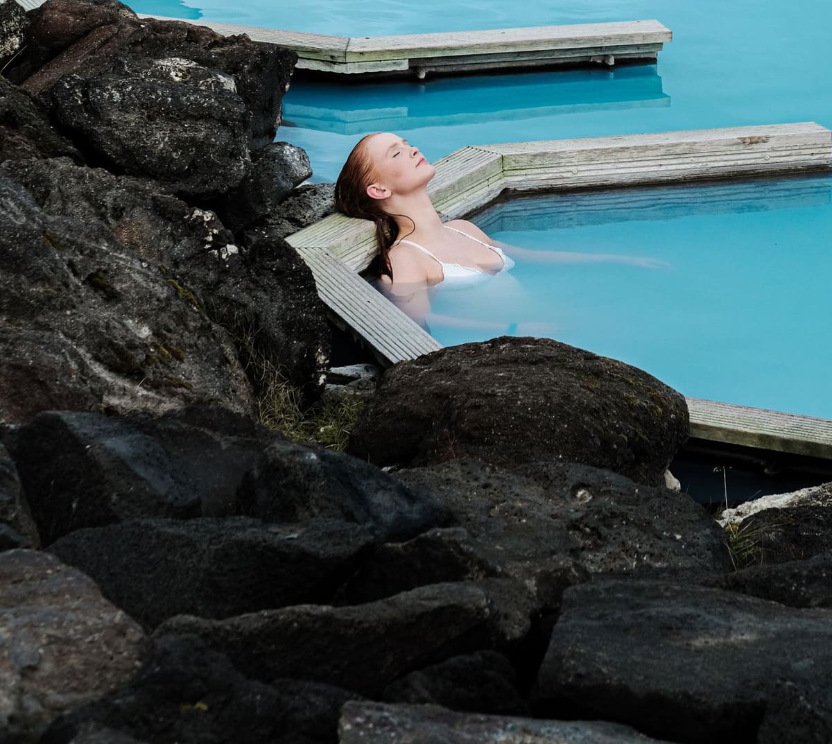 Bather relaxing in blue geothermal water between dark lava rocks at Earth Lagoon Mývatn.