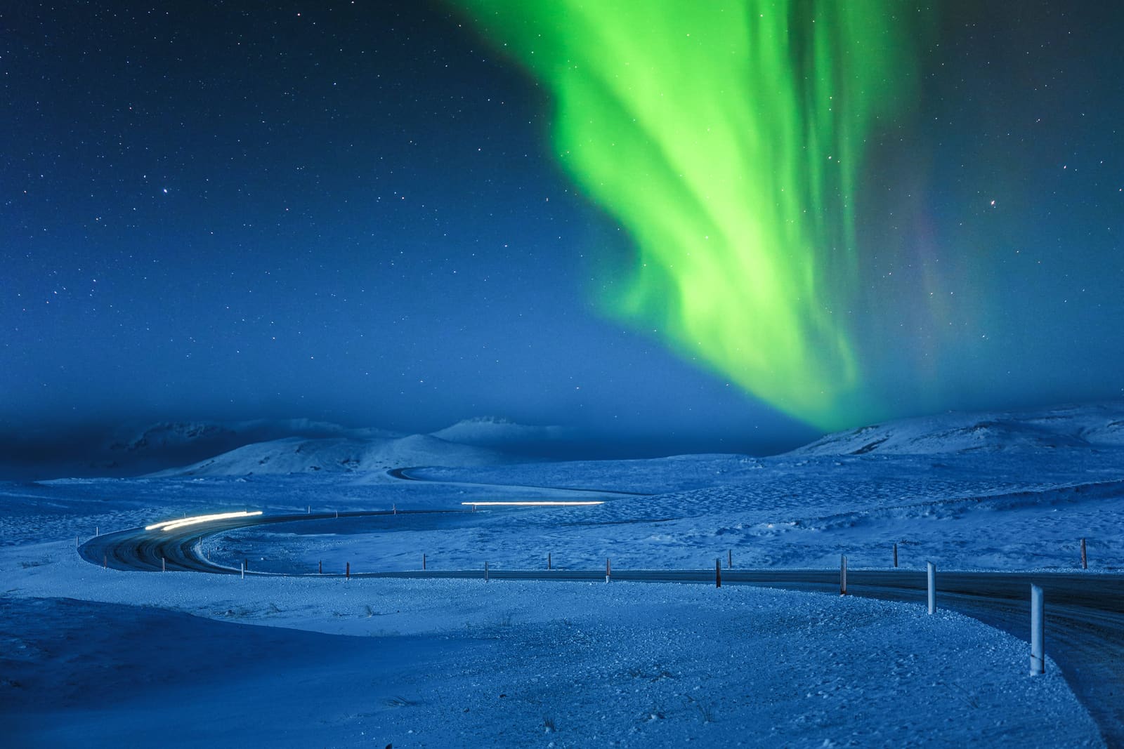 Northern lights glowing above a dark Iceland road.