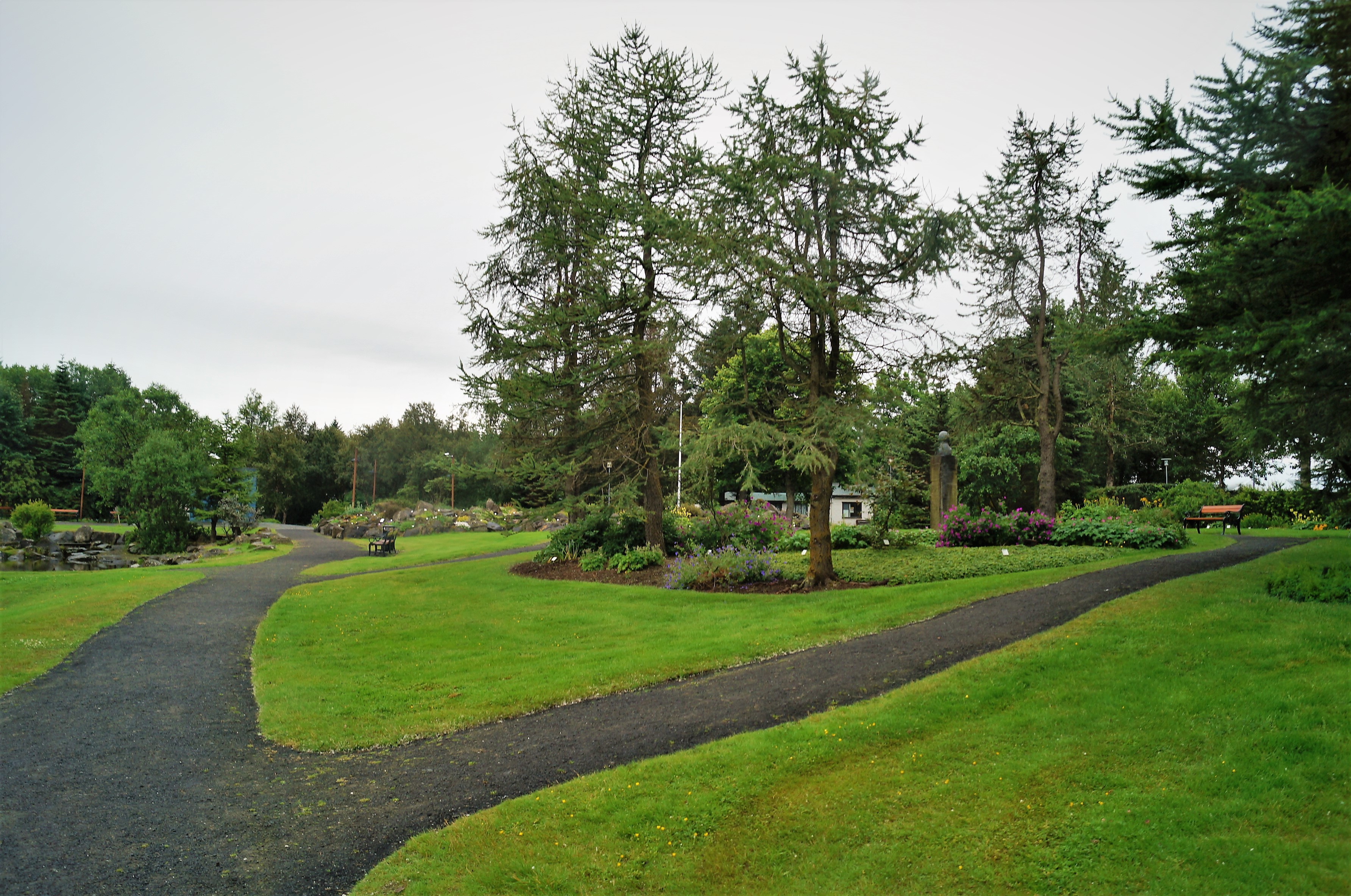Tree-lined walking paths and planted beds inside Reykjavik Botanic Garden.