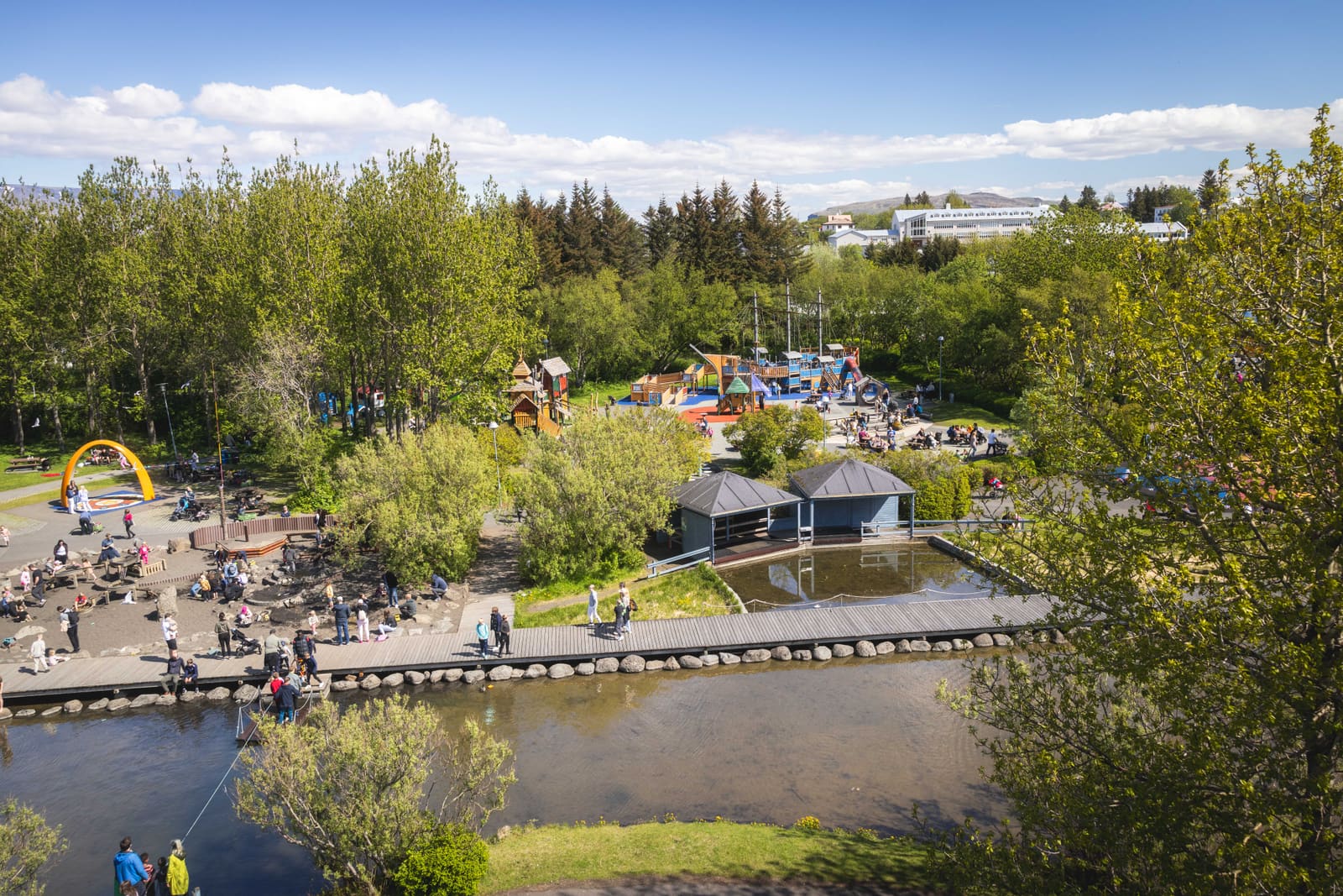Reykjavík Family Park and Zoo seen from above with playgrounds, paths, pond, trees, and families in Laugardalur