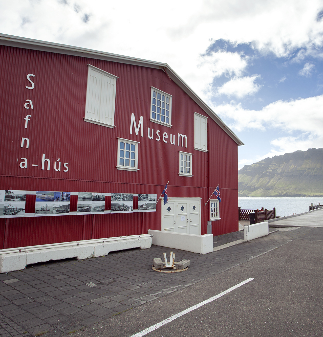 Side view of the red Safnahúsið building in Neskaupstaður with museum signage facing the street.