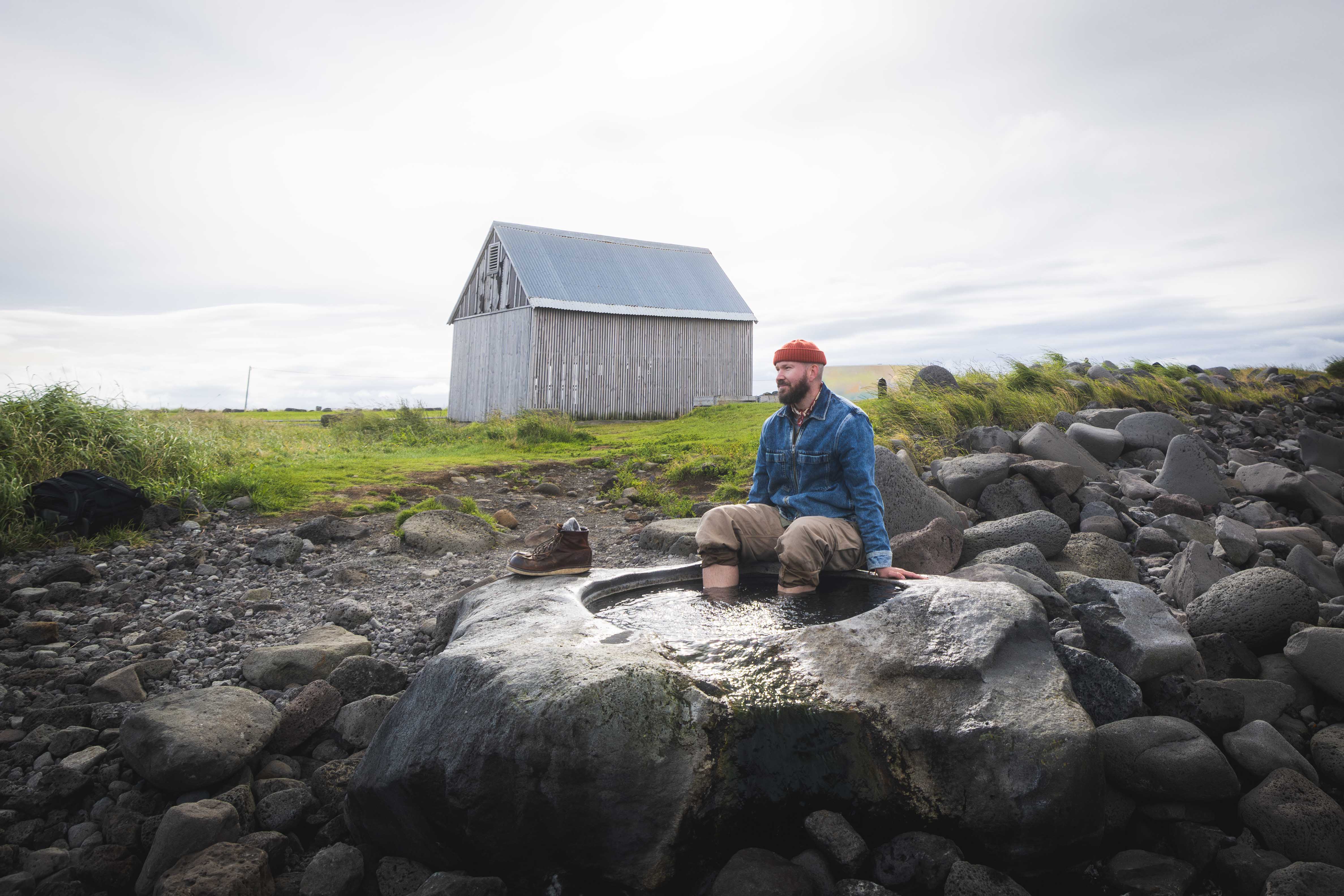 Visitor sitting at Kvika footbath beside the rocky Seltjarnarnes shoreline