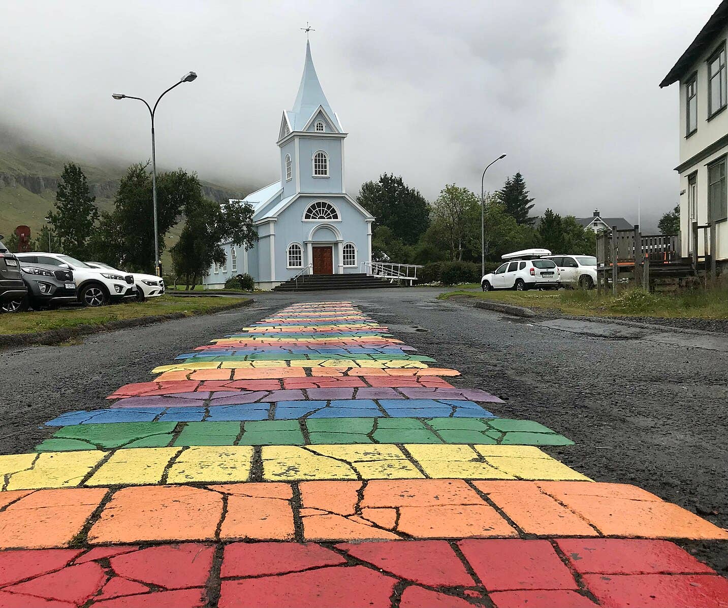 Rainbow Street and Seyðisfjörður Church in wet weather with the blue church framed by low Eastfjords clouds.