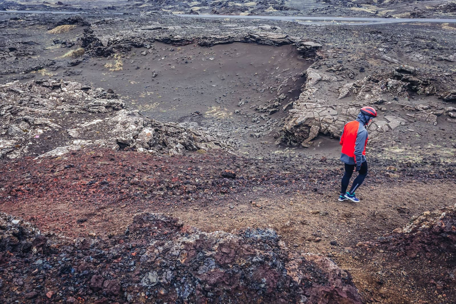 Person walking beside a small crater at Stampar Crater Row on Reykjanes.