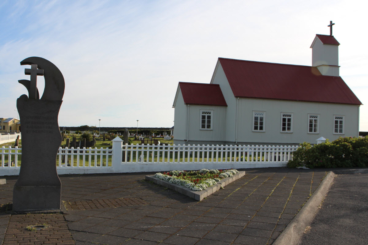 White Stokkseyri church with a red roof behind a low fence and memorial