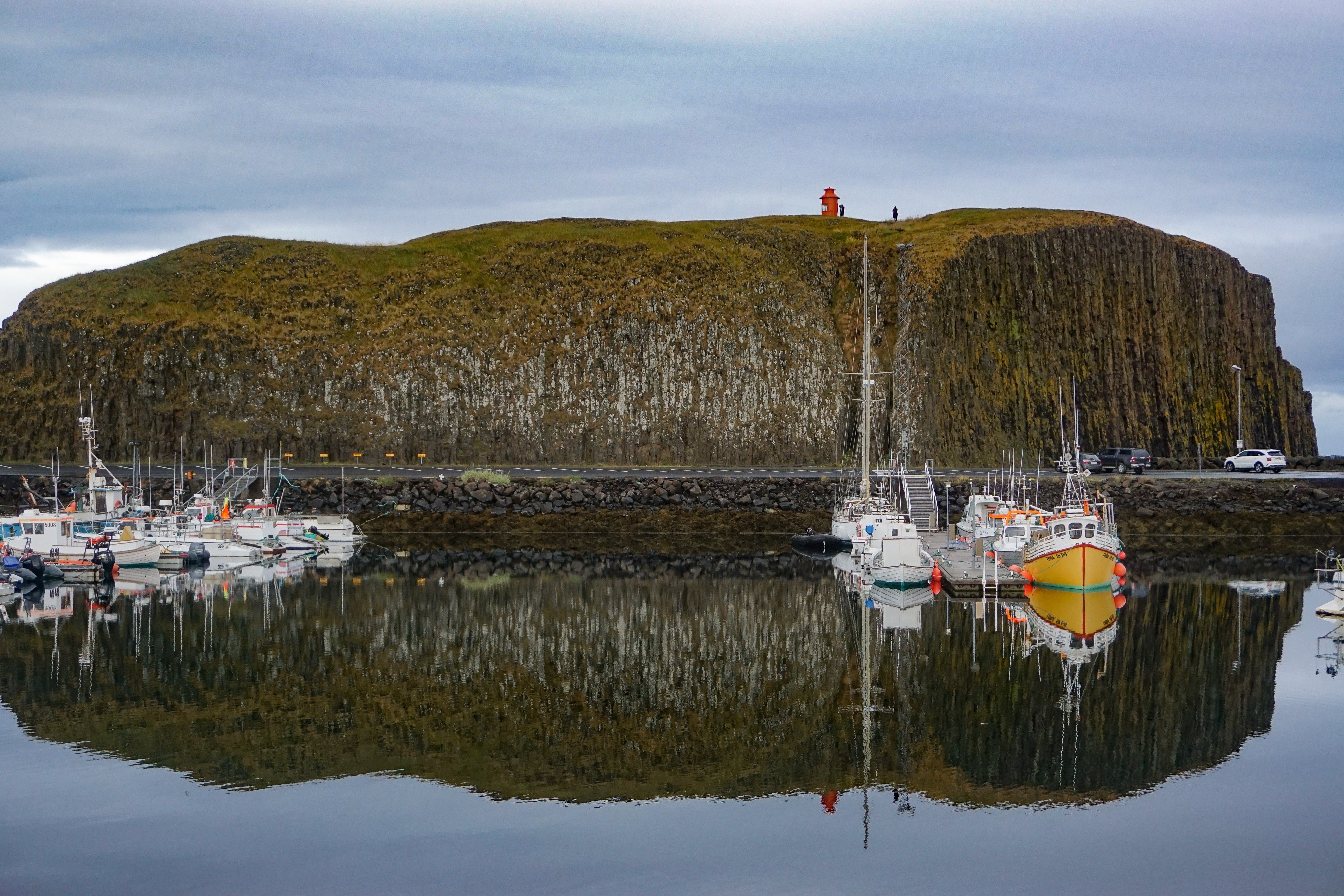 Súgandisey basalt island and red lighthouse above boats in Stykkishólmur harbor.