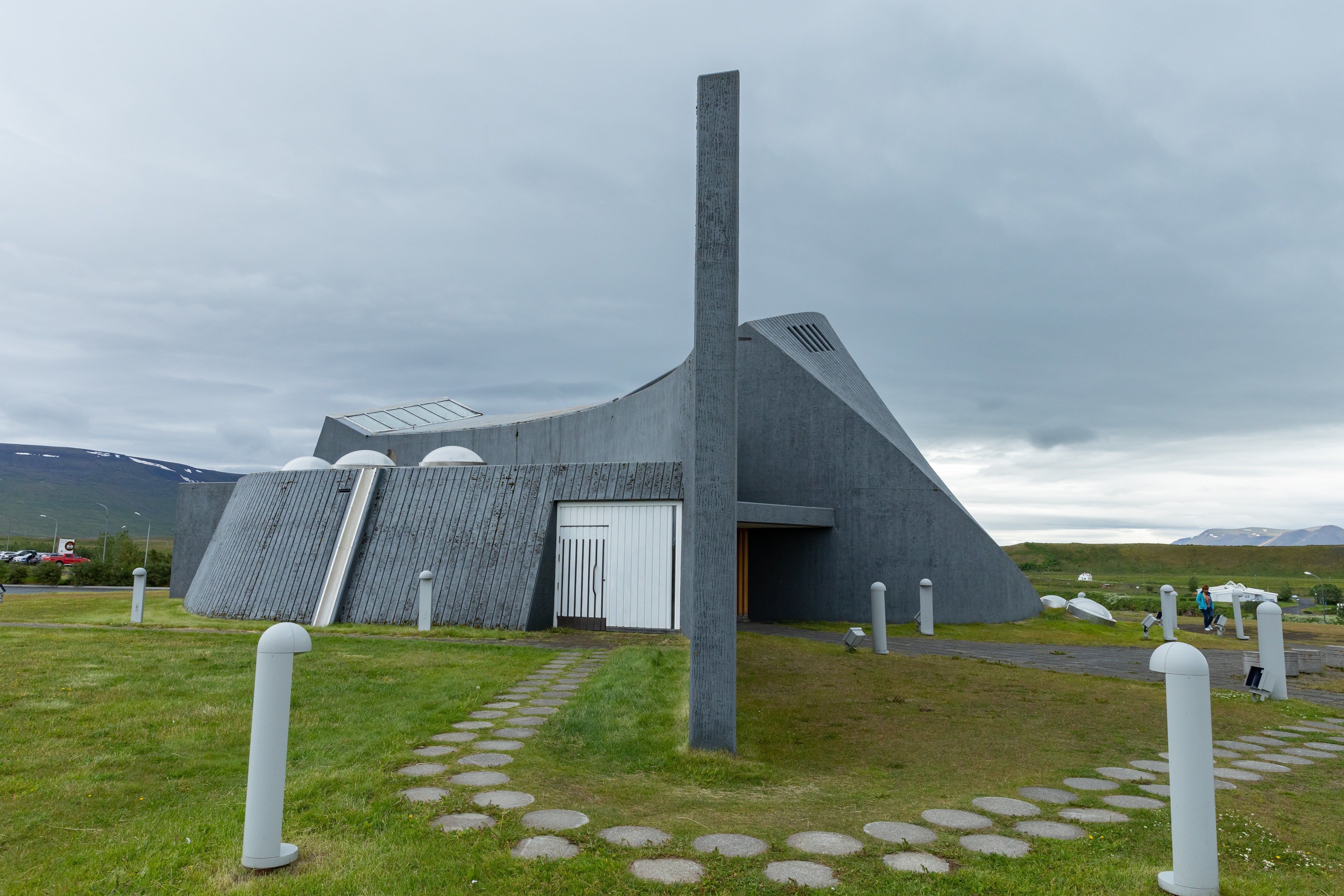 Side view of Stykkishólmskirkja Church showing its concrete walls, tower, and hilltop paths.