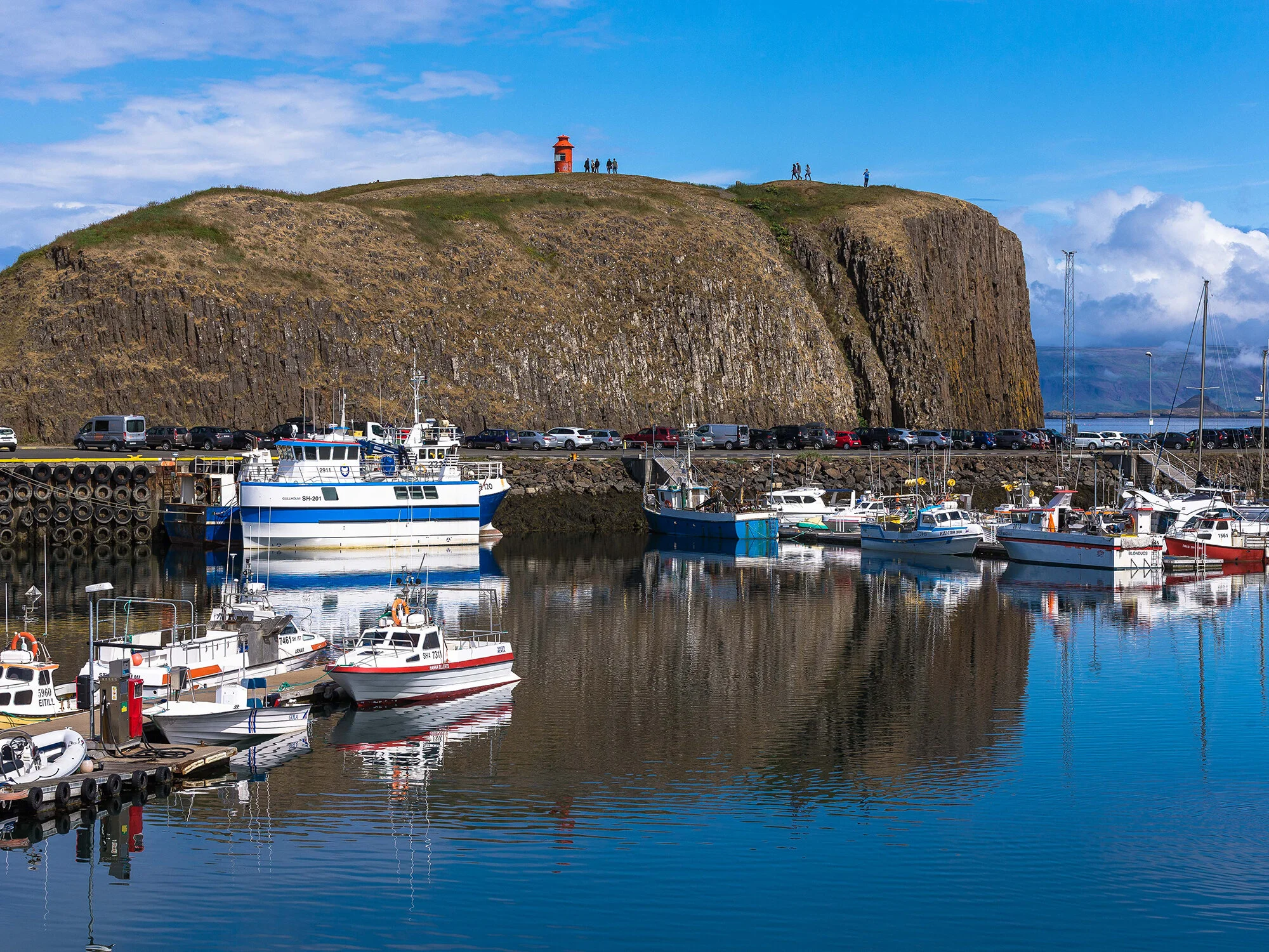 Fishing boats in Stykkishólmur harbor below the Súgandisey cliff and red lighthouse.