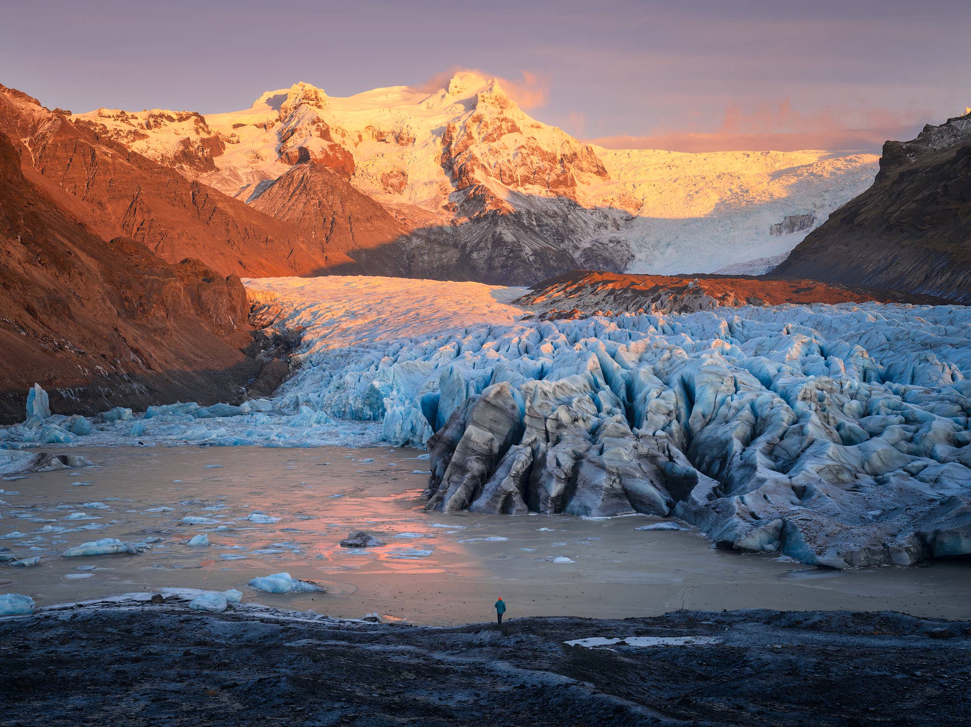 Svínafellsjökull glacier at sunset with blue ice and a person near the glacier lagoon.