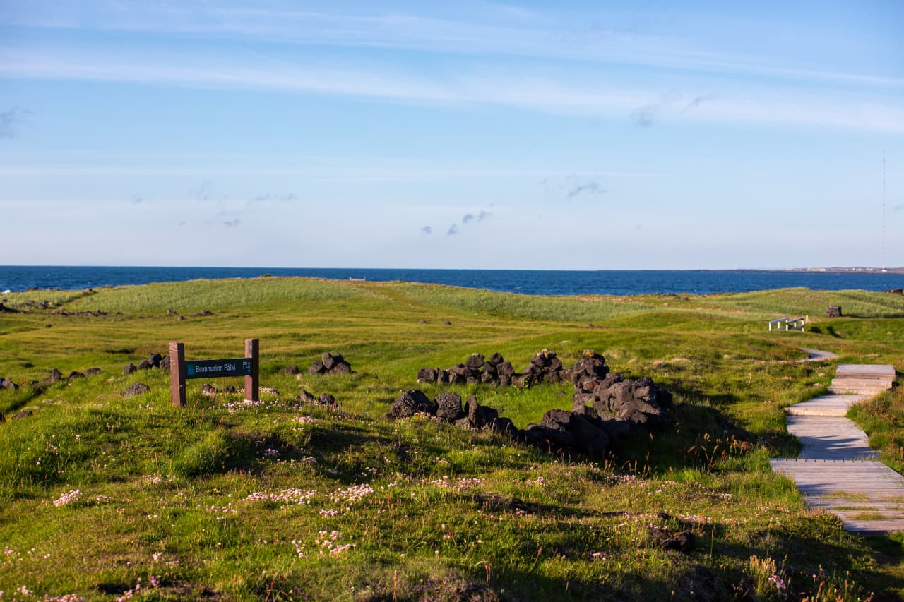 Brunnurinn Fálki sign, low ruins, and boardwalk on the Öndverðarnes side of the cape.