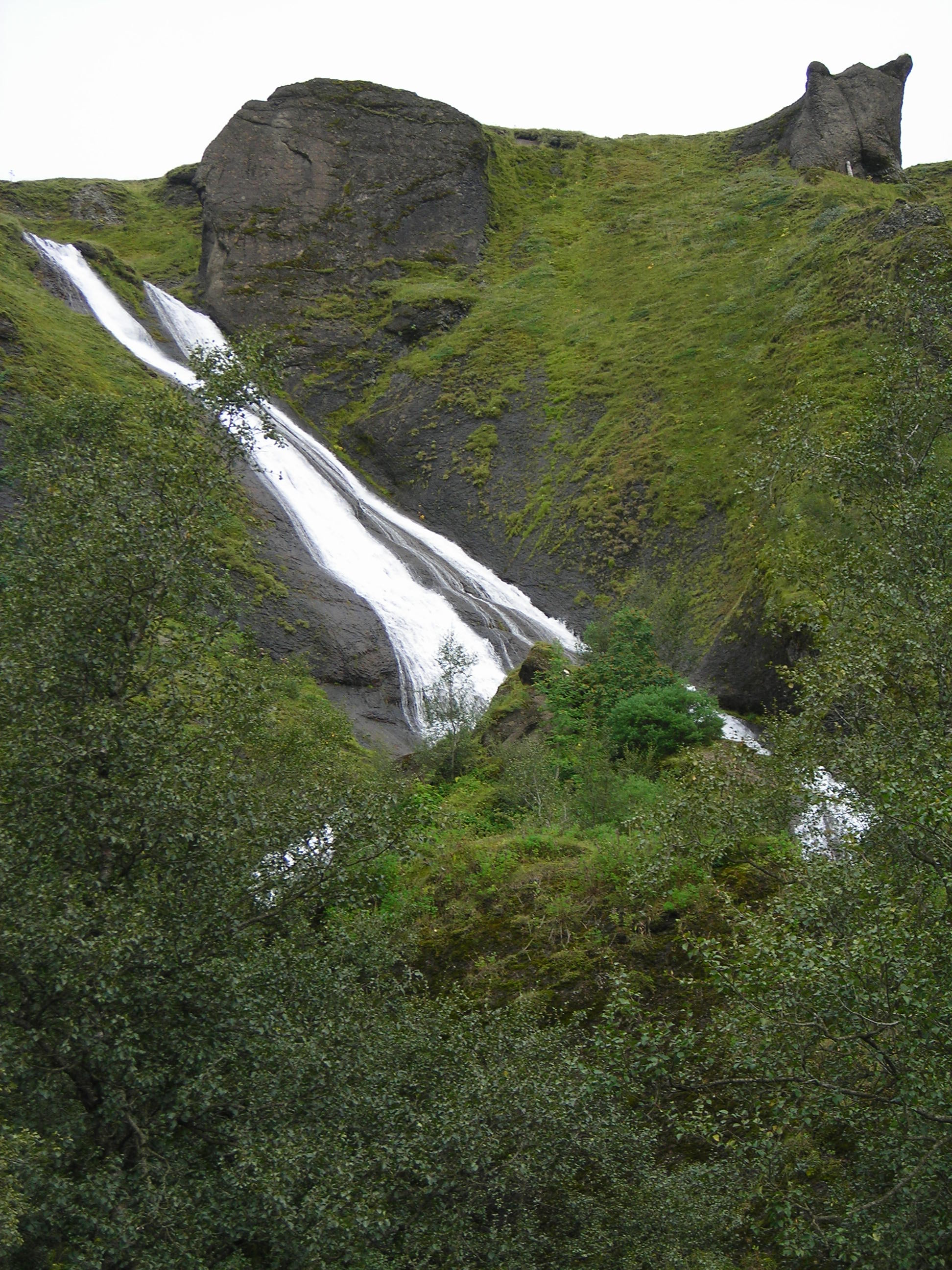 Two streams of Systrafoss running down a green cliff in Kirkjubæjarklaustur.