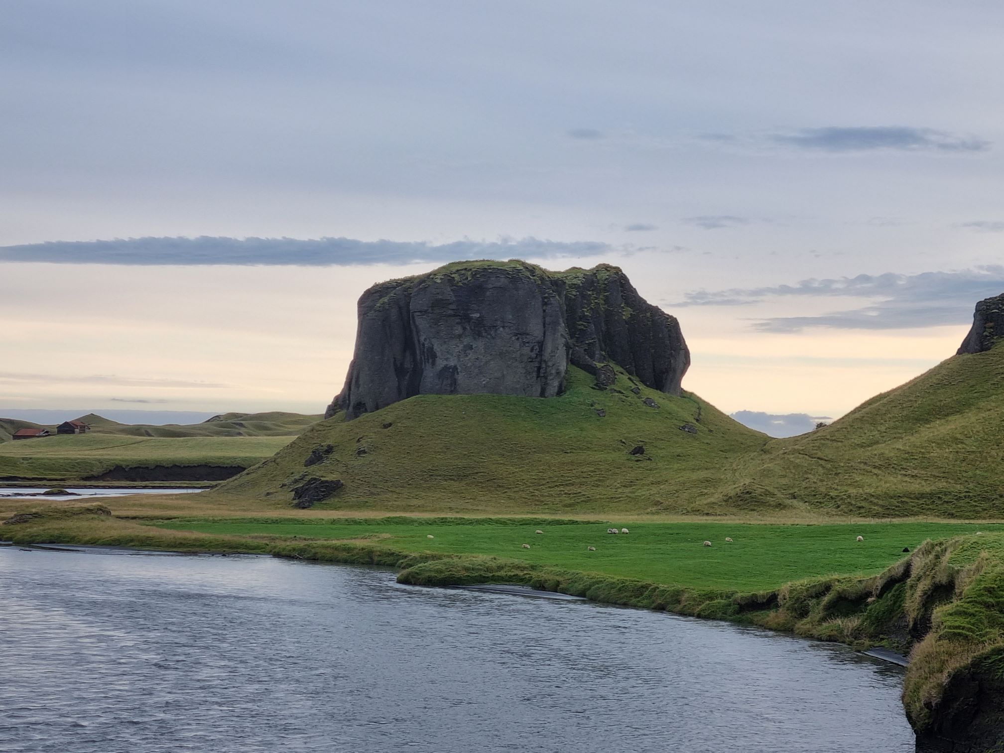 Closer view of Systrastapi above the river with sheep and grassy slopes in the foreground.