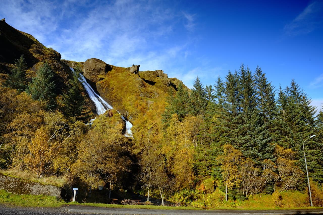 Systrafoss waterfall dropping through the green slope below the ridge near Kirkjubæjarklaustur.