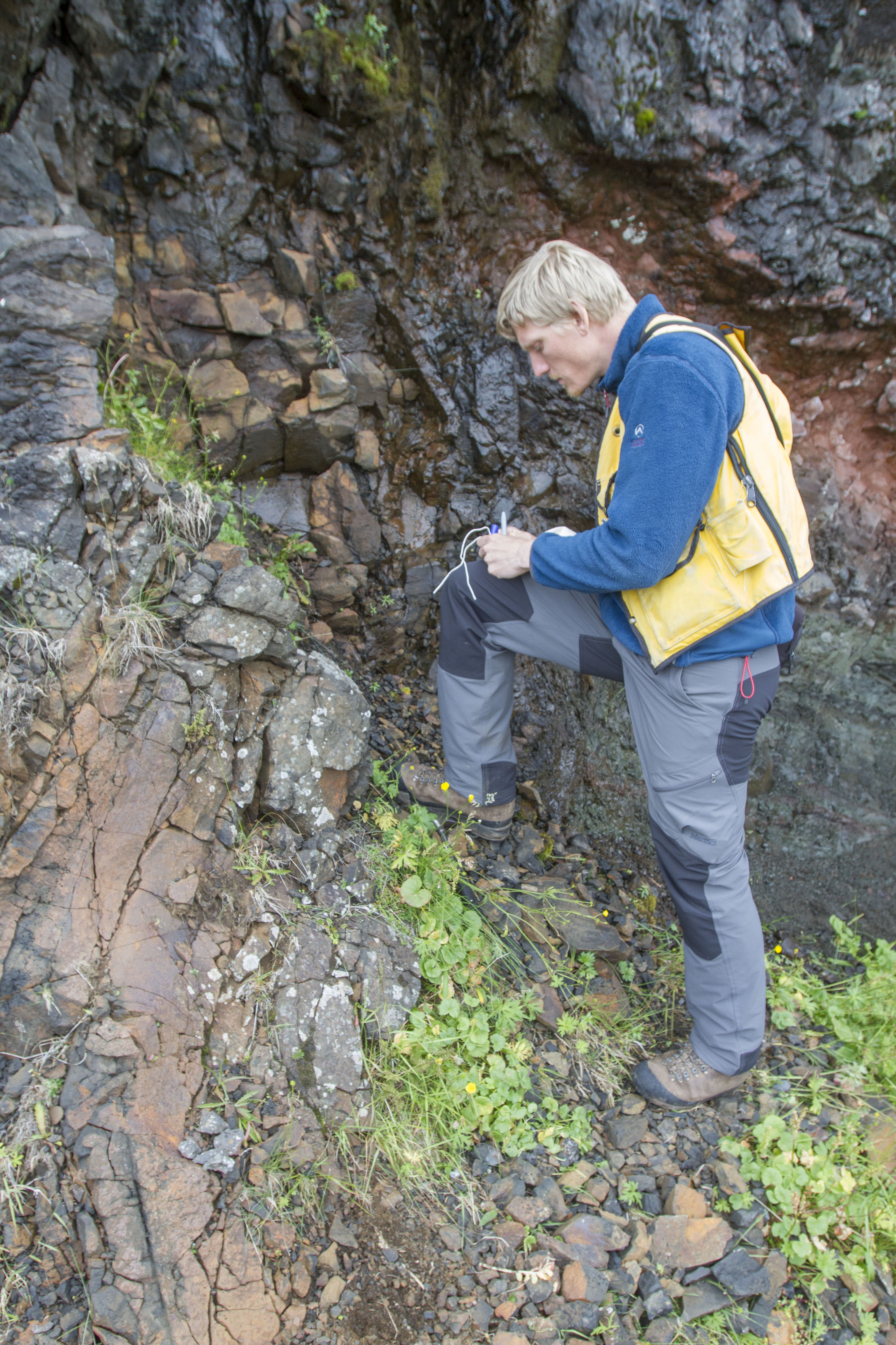 Visitor beside dark Teigarhorn rock layers in East Iceland