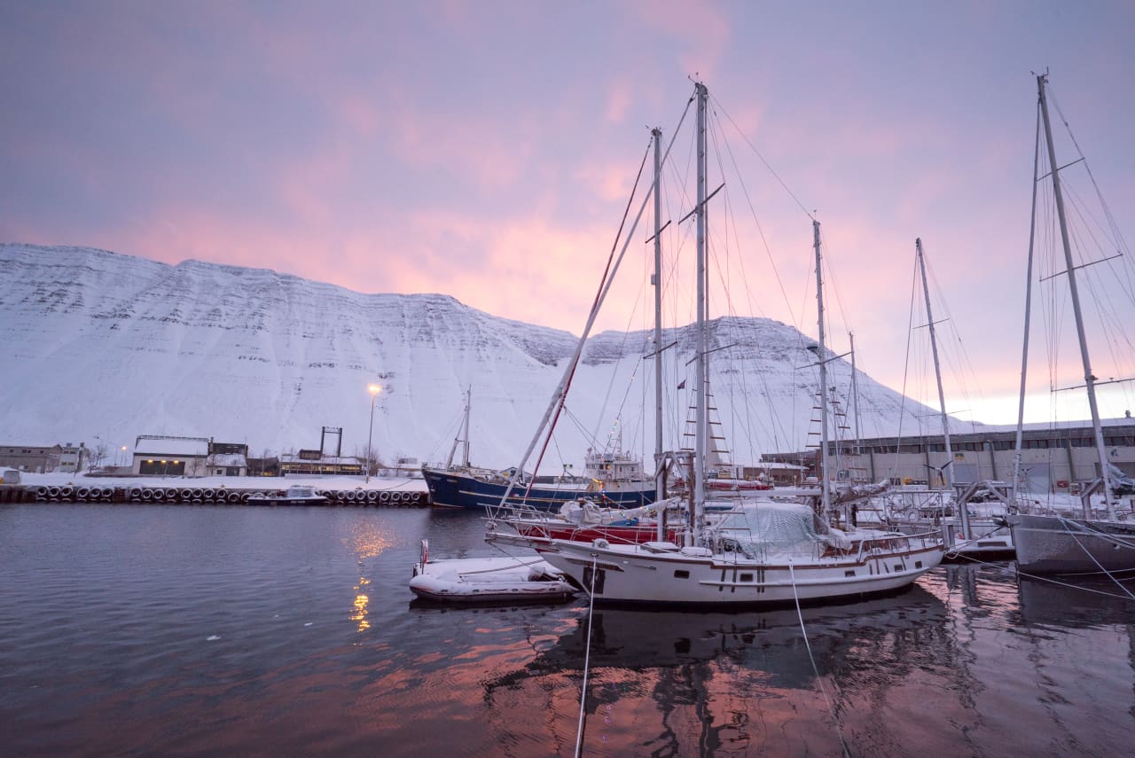 Boats in the harbor at Ísafjörður with snowy mountains behind them.