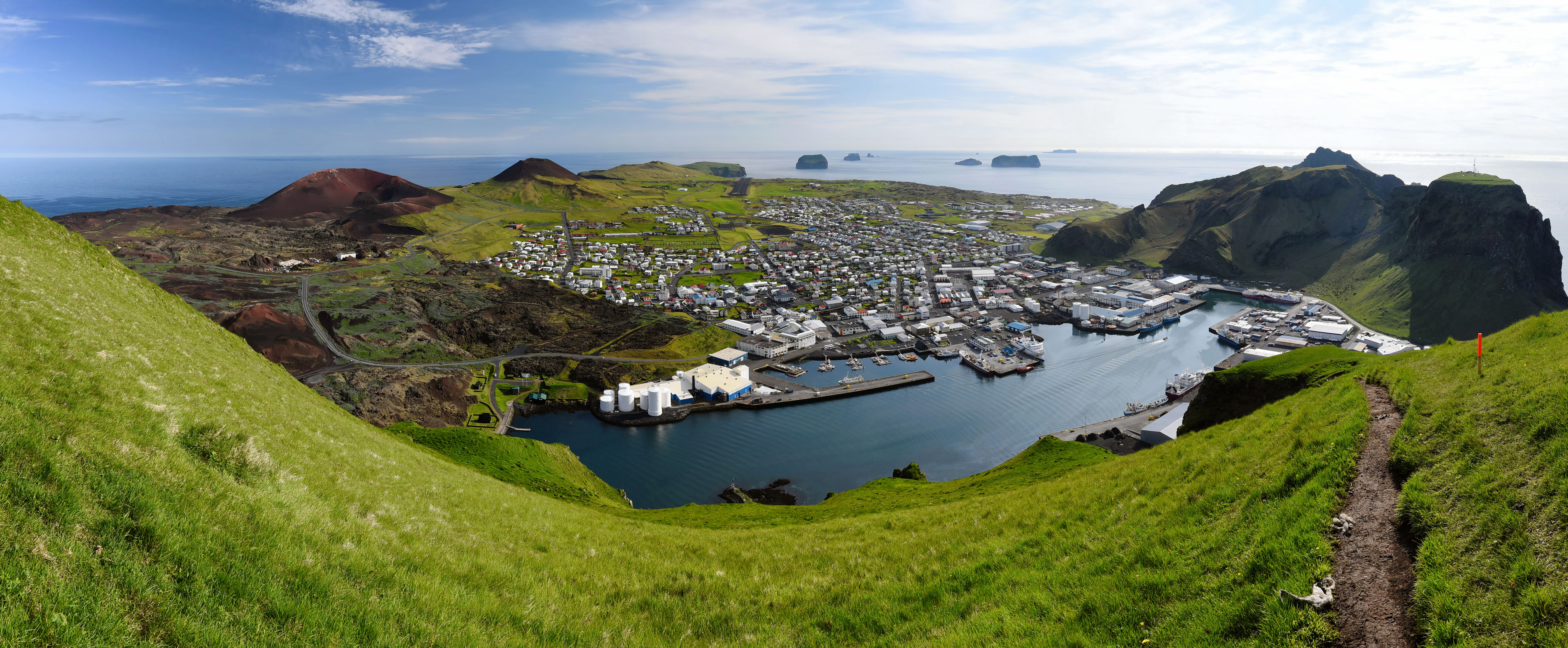 Panoramic view of Heimaey with harbor, town, lava fields, cliffs, and the ocean around the Westman Islands.