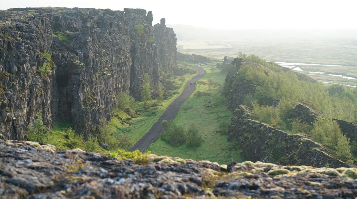 Paved path through Þingvellir rift landscape beside dark rock cliffs