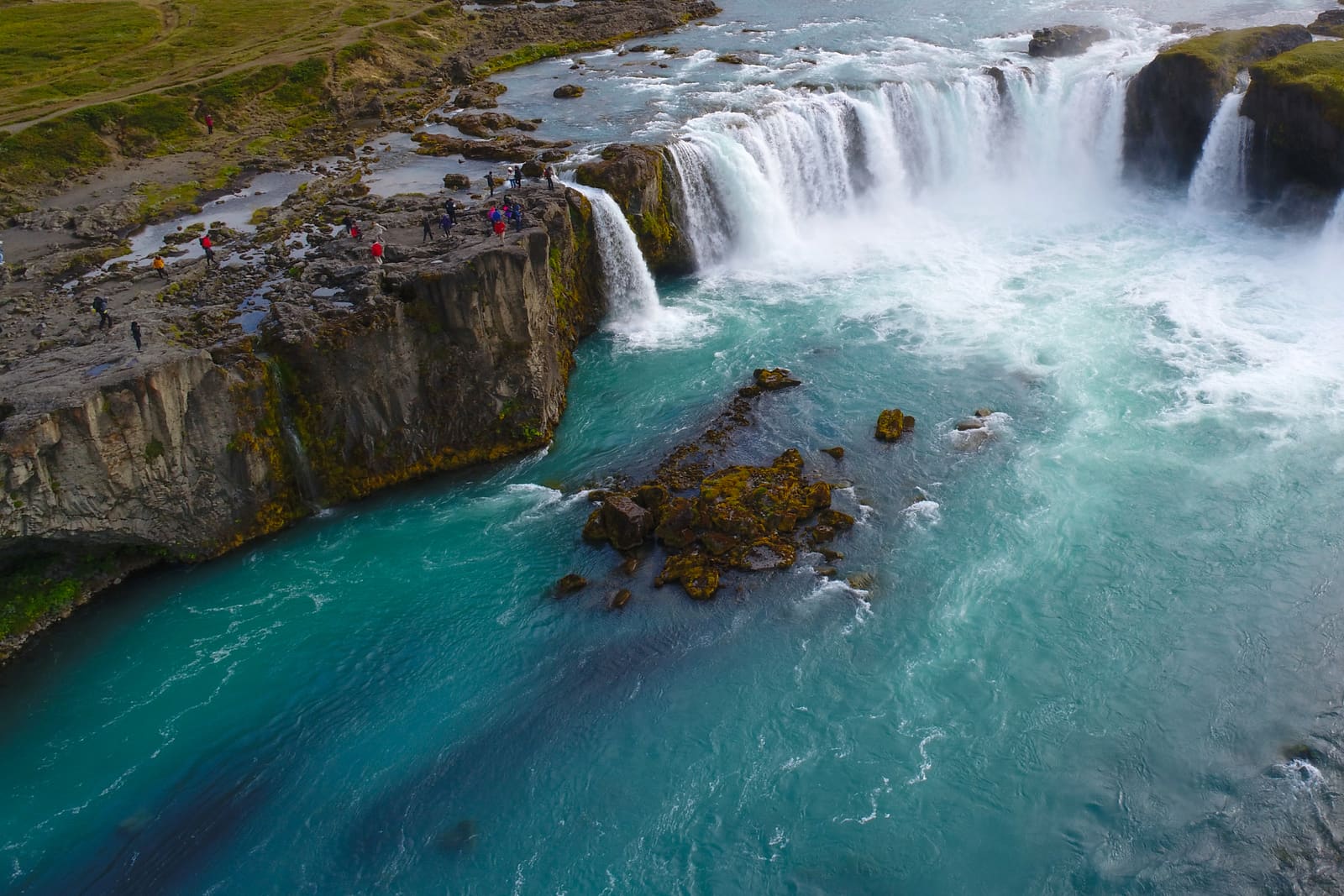 Goðafoss waterfall with visitors along the rocky riverbank