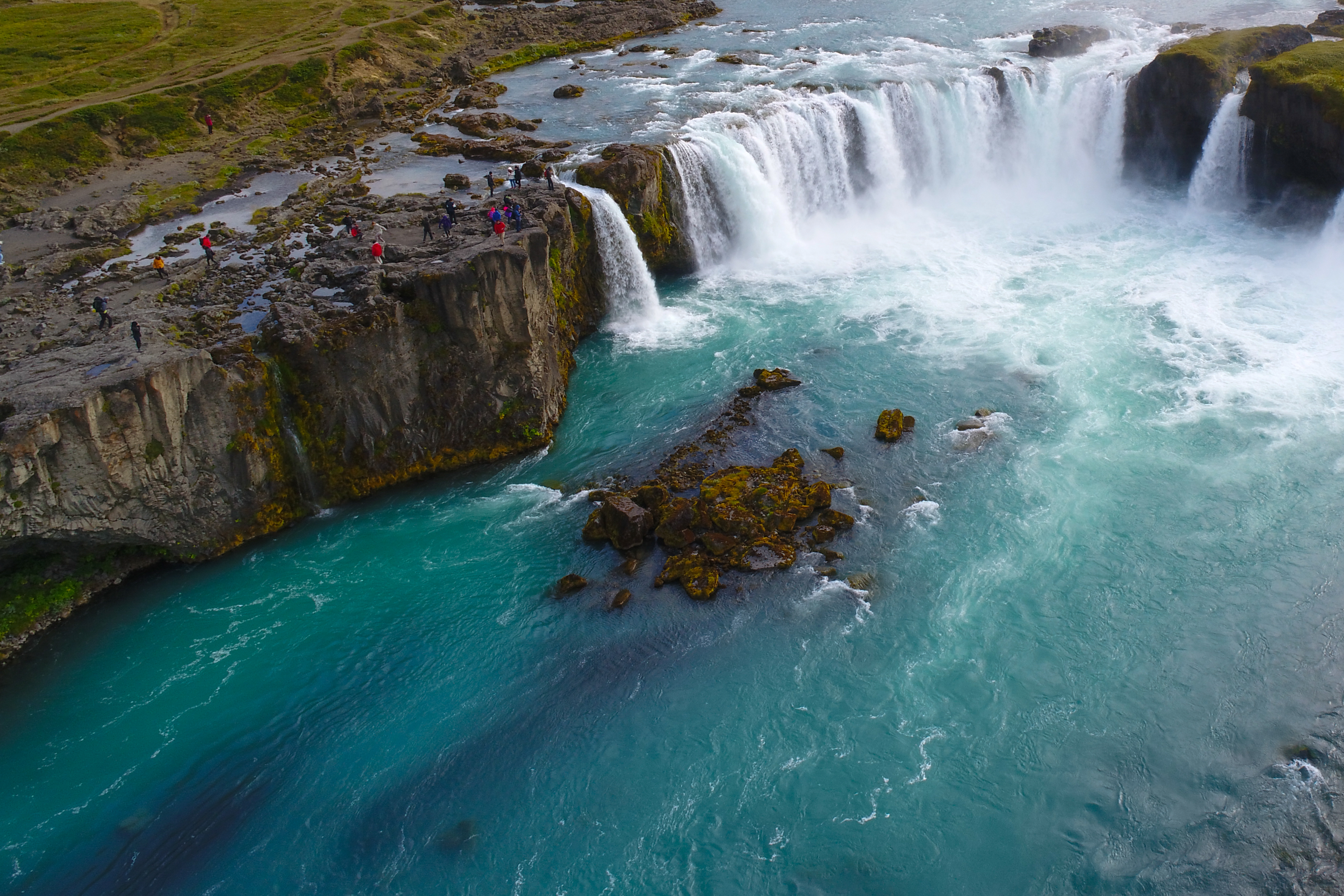 Goðafoss waterfall with visitors along the rocky riverbank