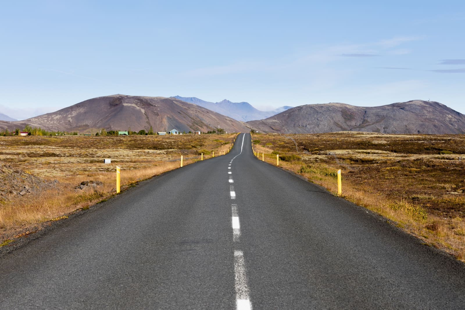 Paved road with yellow roadside posts leading toward mountains in the Golden Circle region