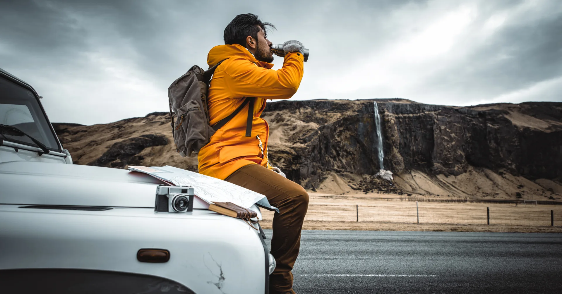 Traveler sitting on a car during a self-drive break on an Iceland route