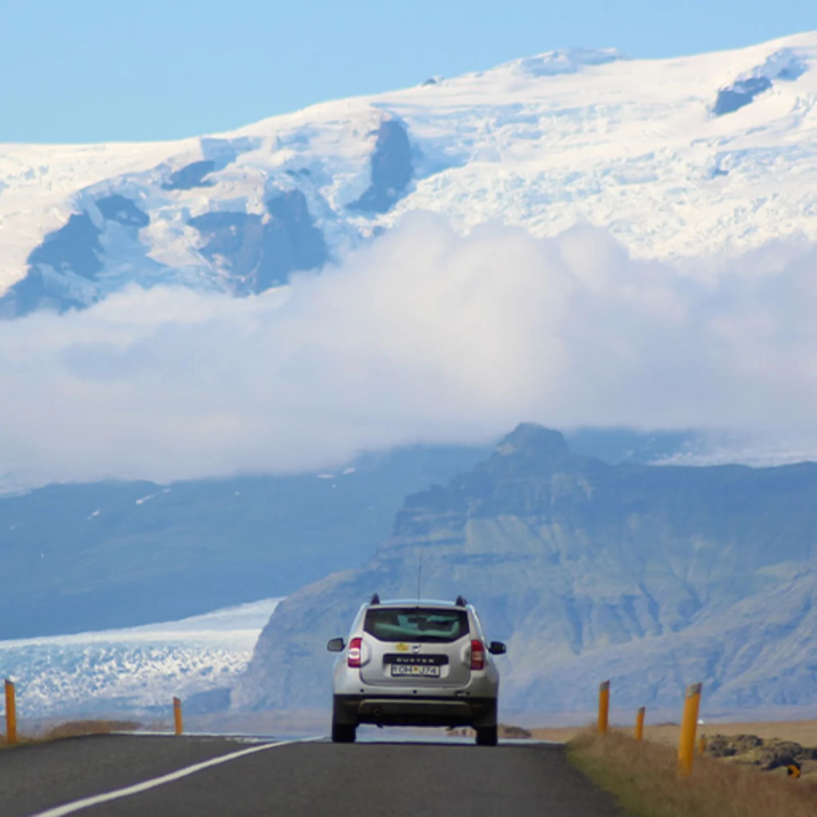 Car on an Iceland road below mountains and a glacier