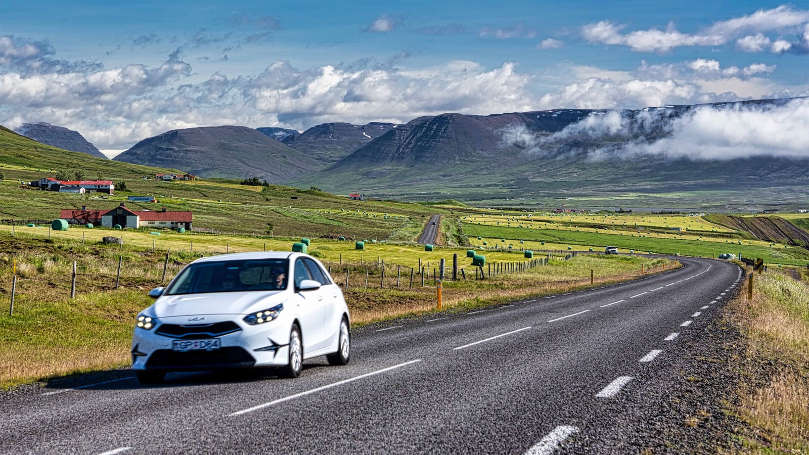 White car on a paved Iceland road with green fields and mountains ahead