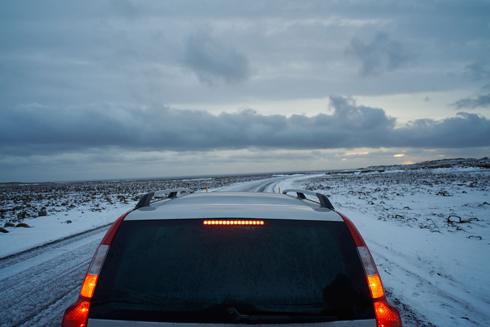 Car ahead on a snow-covered Iceland road under dark clouds