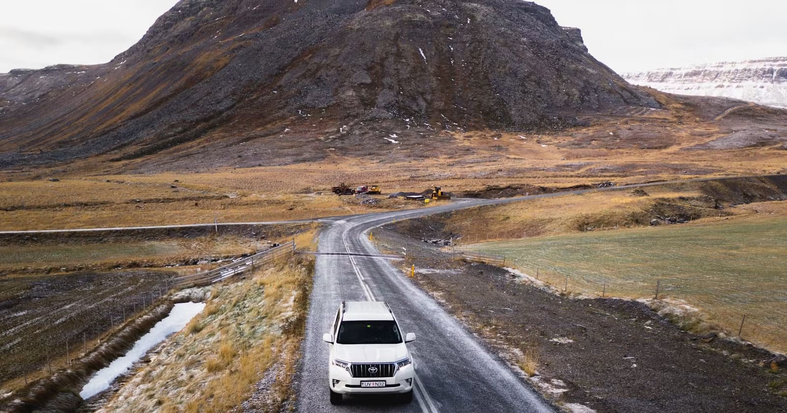 Vehicle driving a paved Iceland road through cold-season rocky terrain
