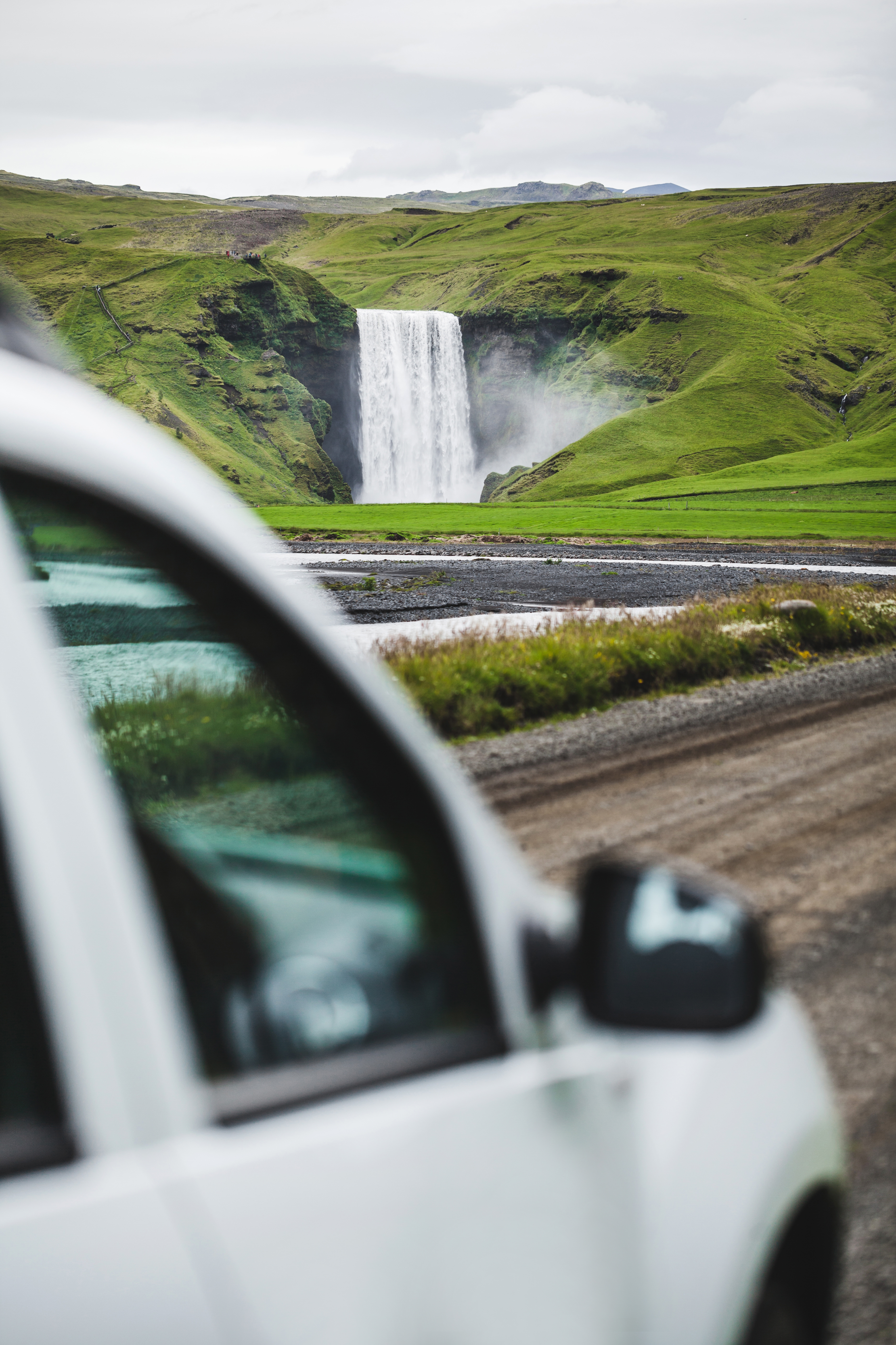 Skógafoss waterfall seen past a car on the South Coast access road