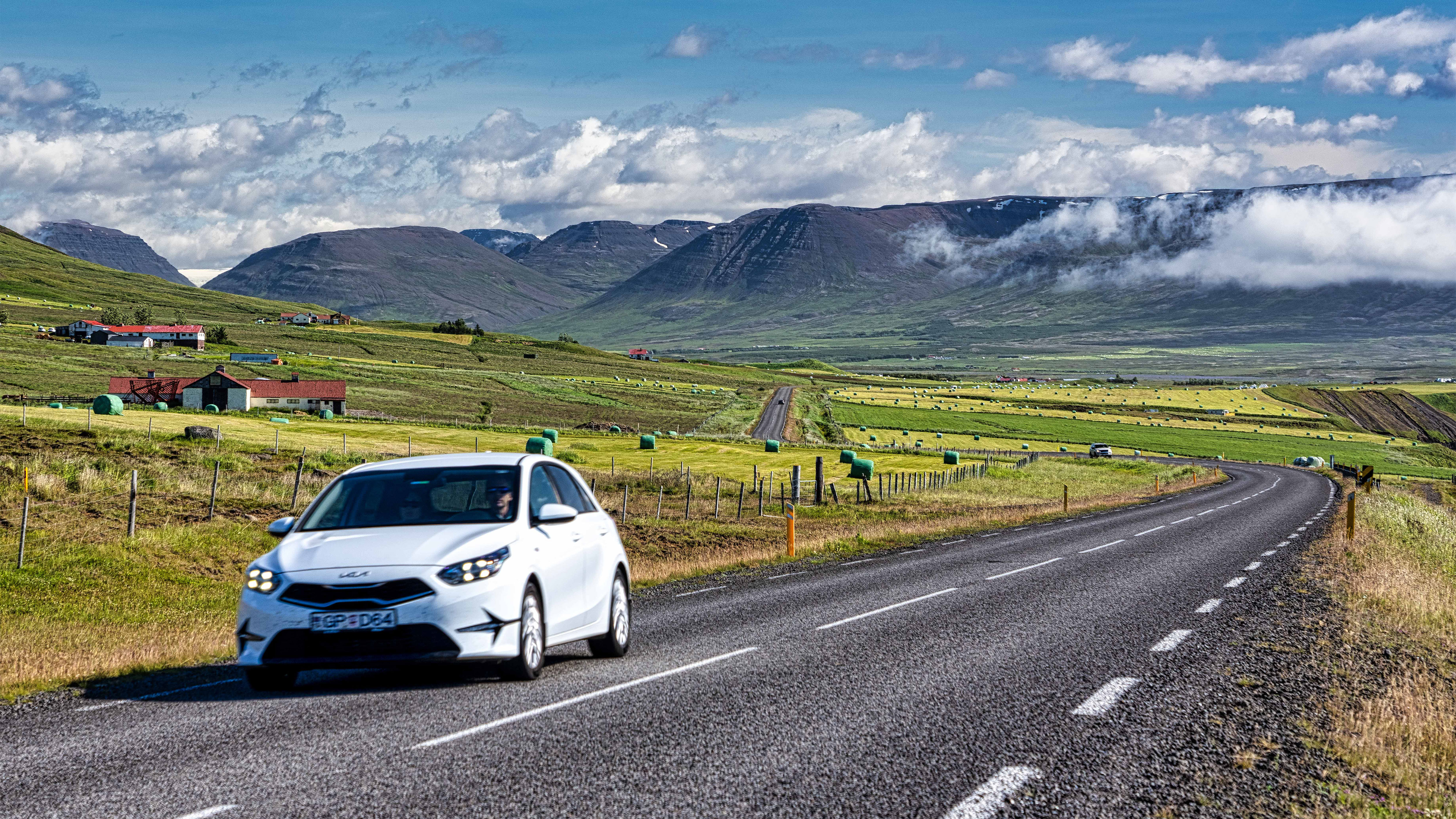 White car on a paved Iceland road with green fields and mountains ahead