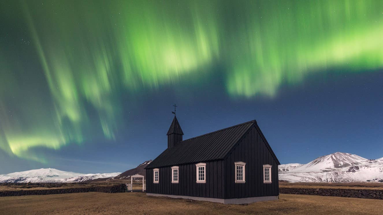 Northern lights glow above the black church at Búðir in winter on Snæfellsnes.