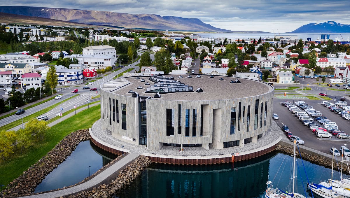 Hof Cultural Centre on the Akureyri waterfront with the town, harbor, and Eyjafjörður behind it.