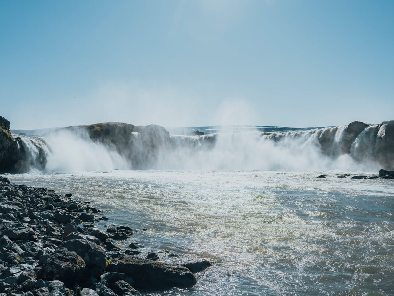 Goðafoss spreading across a rocky ledge with mist rising above the river in North Iceland.