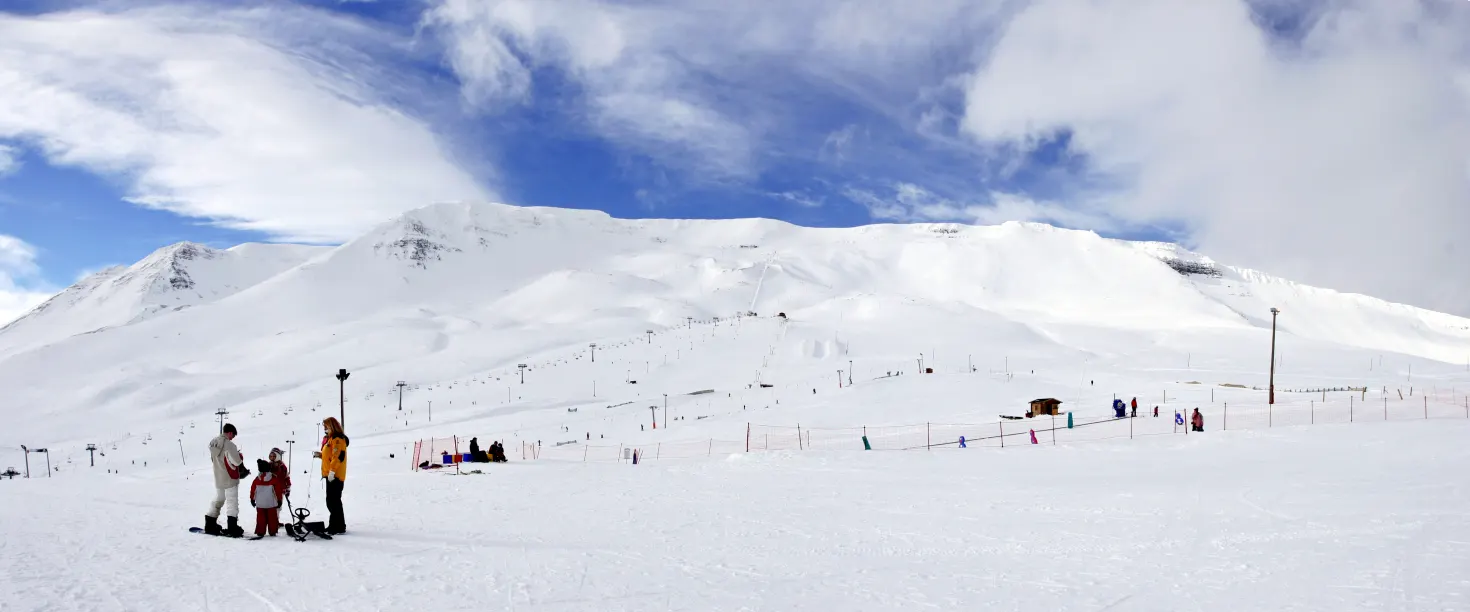 Snow-covered Hlíðarfjall ski terrain above Akureyri with lift lines and visitors below the mountain face.