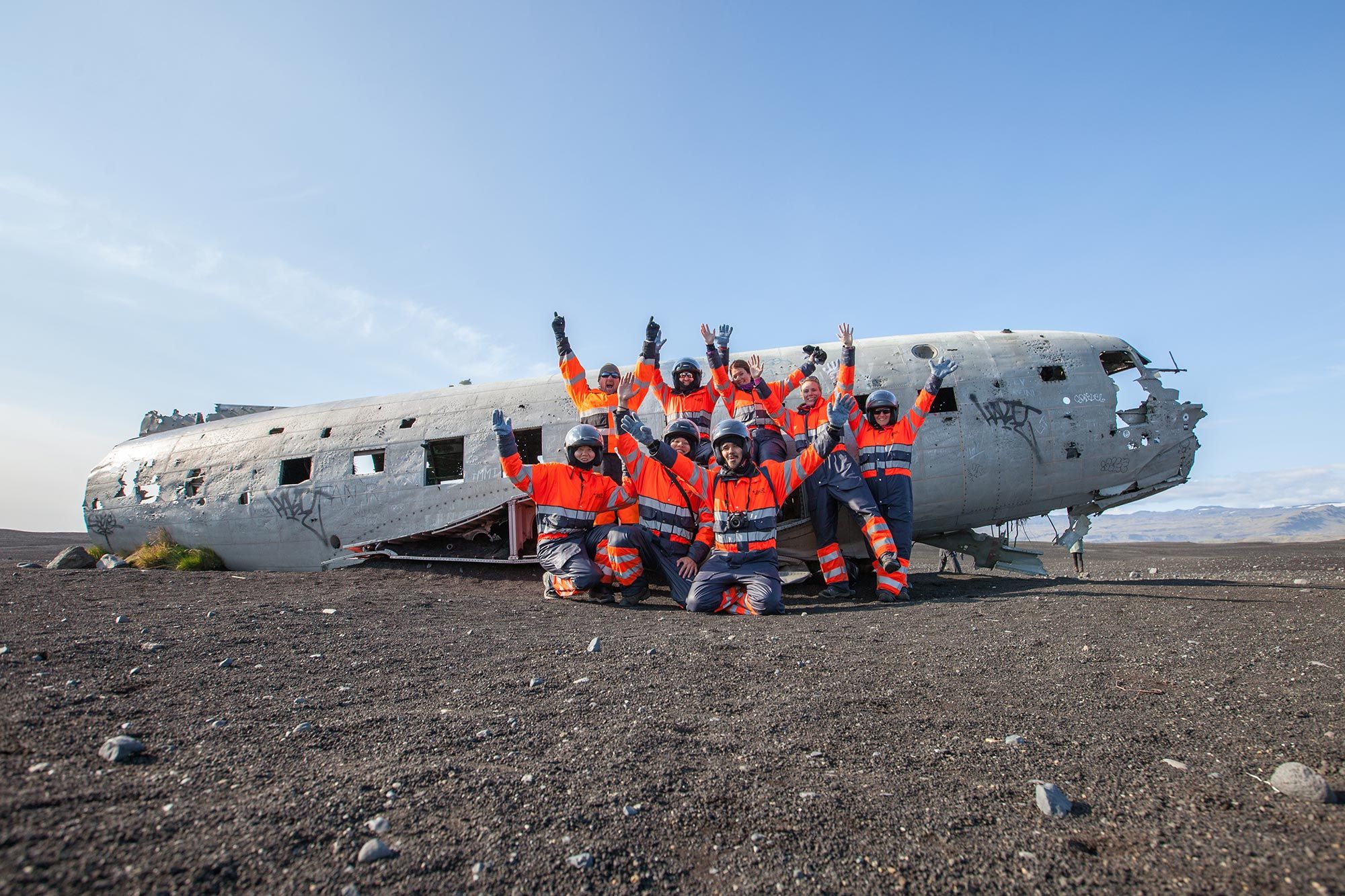 A helmeted ATV group in protective overalls stopped beside the Sólheimasandur plane wreck.