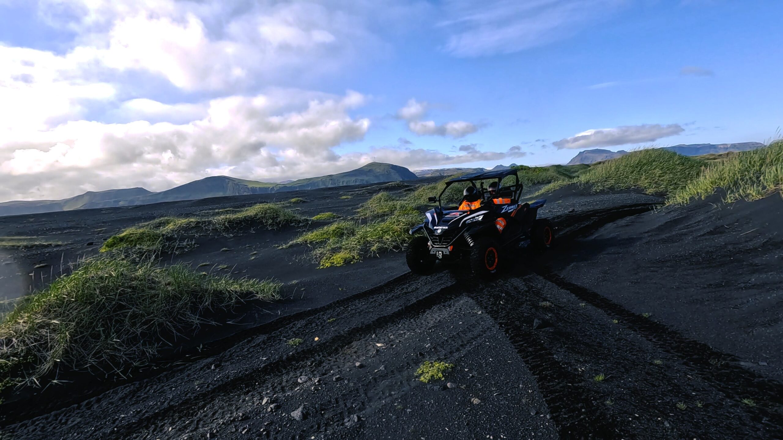 A two-person buggy following an existing wheel track through black-sand terrain near Vík.