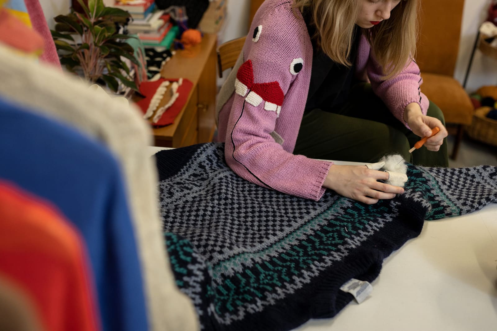 Icelandic textile designer visibly mending a patterned wool sweater by hand